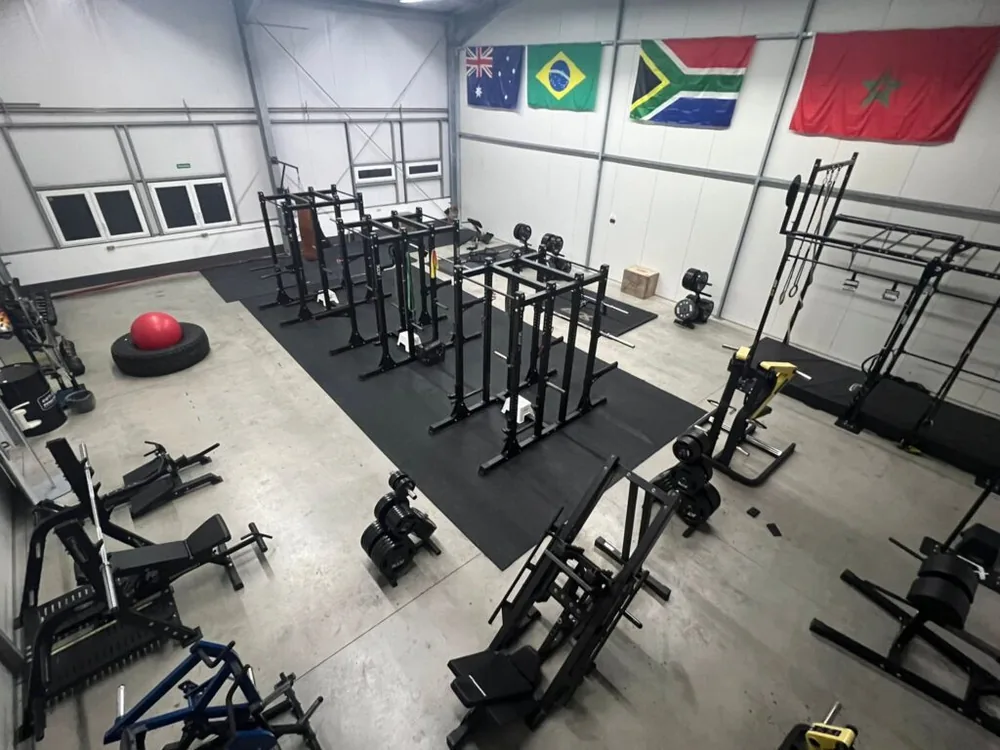 Blick in die Trainingshalle mit mehreren Rigs, Langhanteln und freier Trainingsfläche.