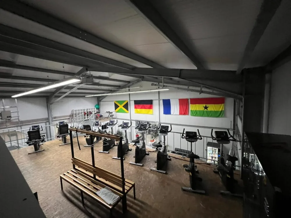 Trainingsfläche mit Holzboden und Geräten unter sichtbaren Stahlträgern.